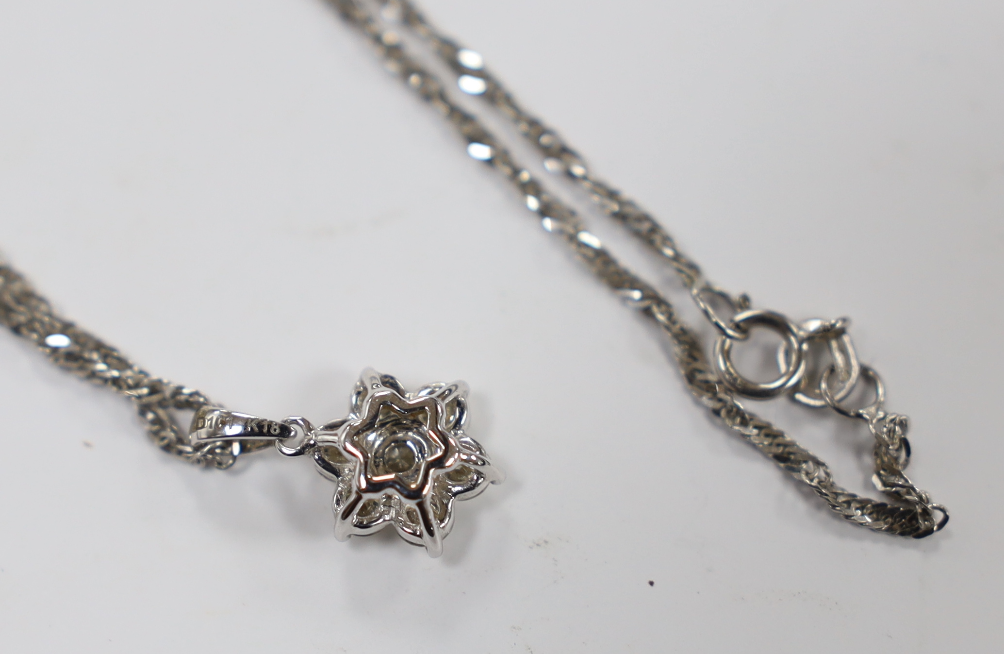 A modern 18k white metal and seven stone diamond cluster set flower head pendant, overall 15mm, on a 9ct white gold chain, 45cm, gross weight 3.2 grams.